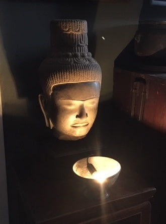 Vishnu sculpture with a serene expression next to a lit candle on a dark wooden surface.